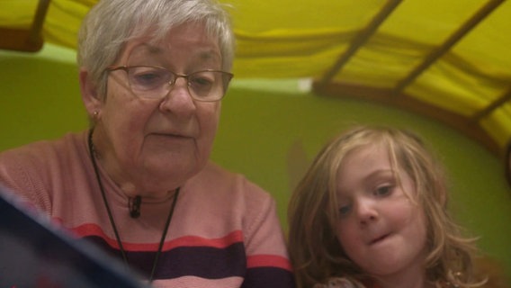 Eine Seniorin liest kleineren Kindern aus einem Buch vor. © Screenshot 