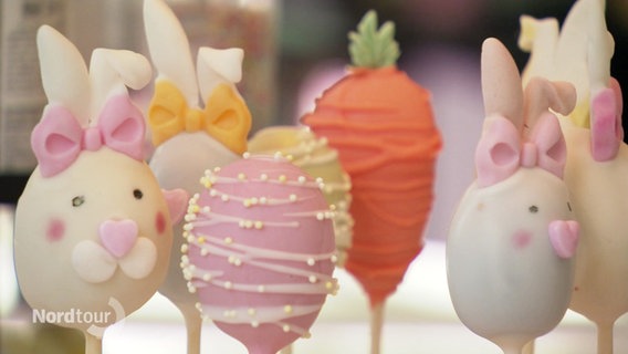 Bunt dekorierte, zu Osteiern und Osterhasen geformte Cake-Pops stehen auf Sielen bei einander. © Screenshot 