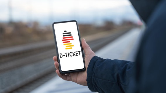 Eine Person steht an einem Bahnsteig und hält in der Hand ein Smartphone in der Hand, auf dem ein Deutschlandticket ist. © picture alliance / CHROMORANGE | Michael Bihlmayer Foto: Michael Bihlmayer